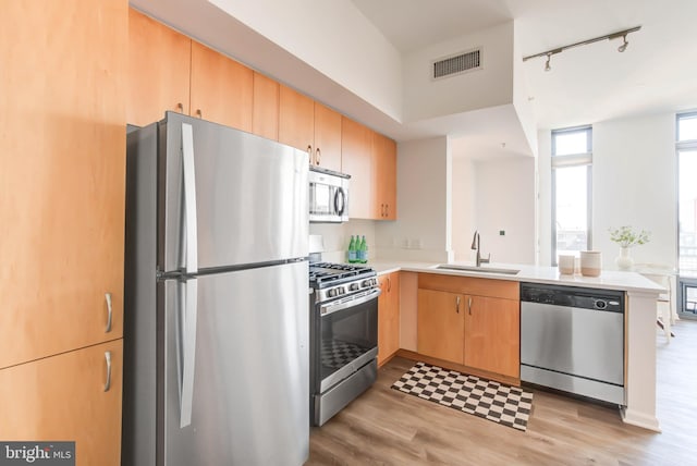 kitchen with light brown cabinetry, appliances with stainless steel finishes, light wood-style floors, a sink, and a peninsula