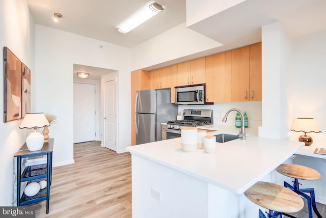 kitchen featuring stainless steel appliances, light countertops, light brown cabinets, a peninsula, and a kitchen breakfast bar