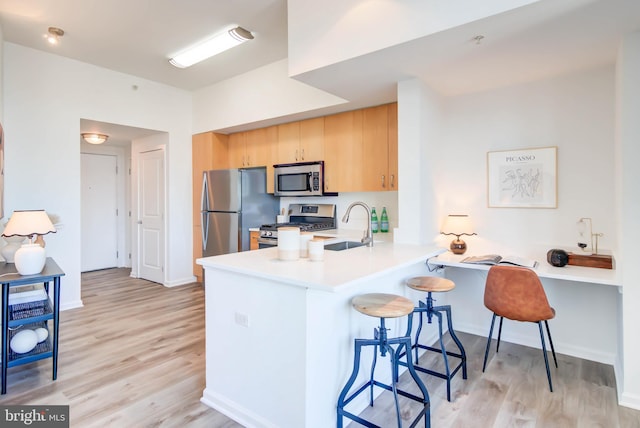 kitchen featuring a breakfast bar area, a peninsula, a sink, appliances with stainless steel finishes, and light brown cabinetry