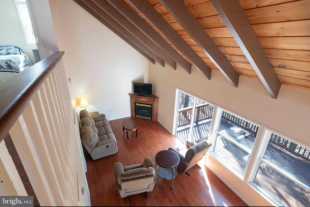 living area with vaulted ceiling with beams, wood finished floors, a glass covered fireplace, and wood ceiling