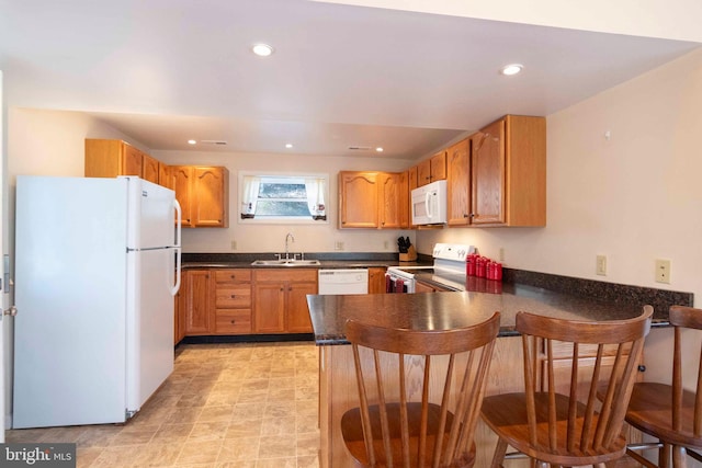 kitchen with recessed lighting, a peninsula, white appliances, a sink, and dark countertops