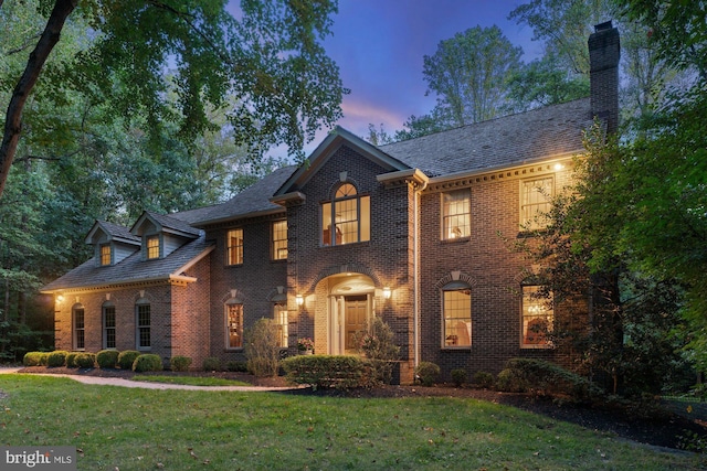 georgian-style home with brick siding, a lawn, a chimney, and a high end roof