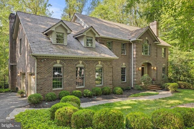 view of front of property featuring aphalt driveway, an attached garage, brick siding, a chimney, and a high end roof