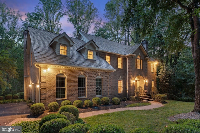 view of front facade with driveway, a yard, a high end roof, and brick siding