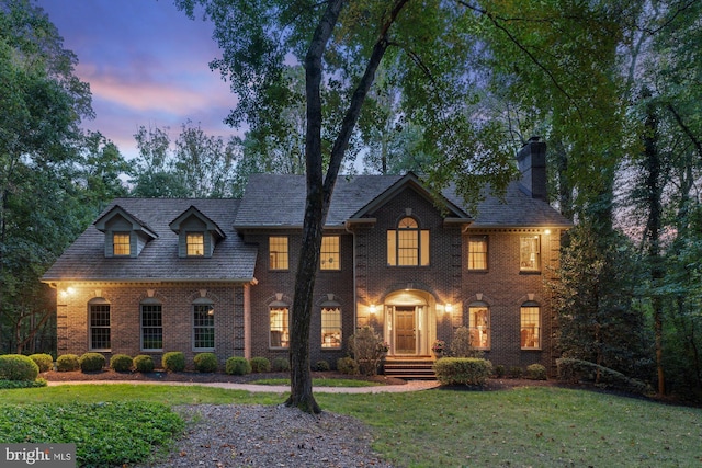 colonial home featuring a front yard, a chimney, a high end roof, and brick siding