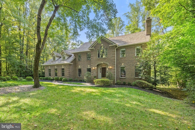 georgian-style home with a front yard, brick siding, and a chimney