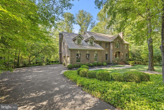 view of front facade with driveway, brick siding, and a chimney