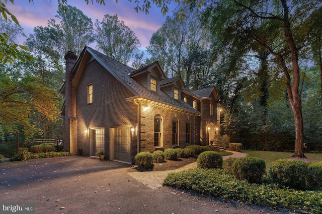 view of side of property featuring a garage, a chimney, aphalt driveway, and brick siding