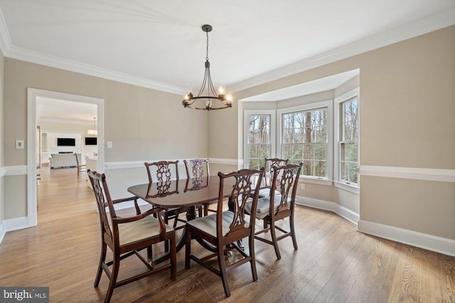 dining space featuring baseboards, ornamental molding, wood finished floors, and a notable chandelier