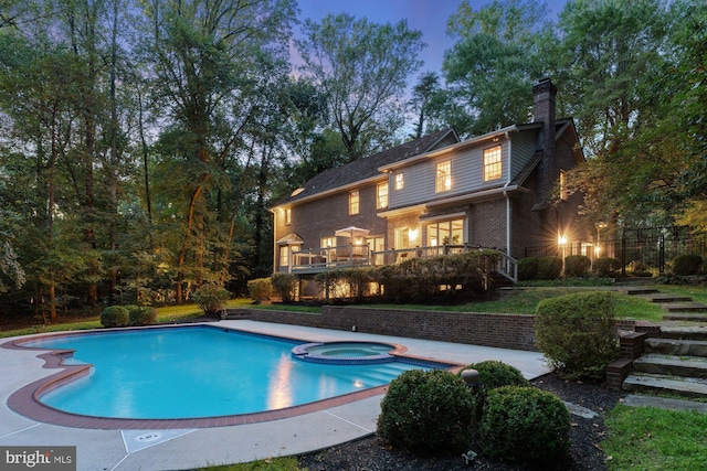 rear view of property featuring a chimney, stairway, a deck, a pool with connected hot tub, and brick siding