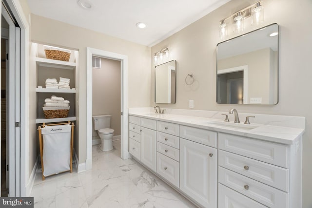 full bathroom with marble finish floor, double vanity, a sink, and toilet