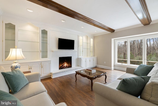 living room featuring wood finished floors, baseboards, ornamental molding, a brick fireplace, and beamed ceiling