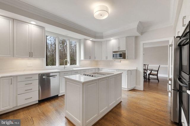 kitchen featuring stainless steel appliances, a sink, light wood-style floors, light countertops, and ornamental molding