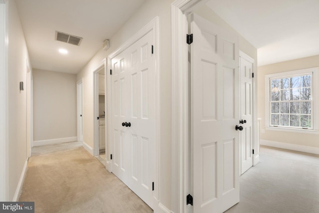 hallway with light colored carpet, visible vents, and baseboards