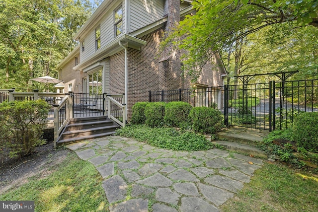 view of side of property with a deck, brick siding, and fence