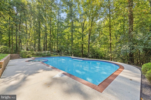 view of swimming pool featuring a patio, a forest view, and a pool with connected hot tub