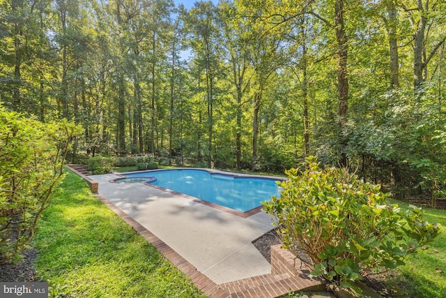 view of swimming pool featuring a pool with connected hot tub, a patio area, and a forest view