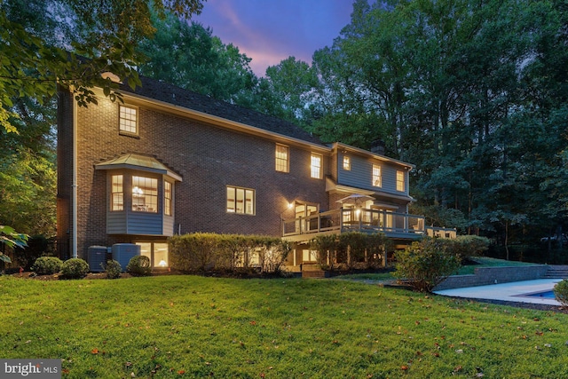 back of house at dusk featuring central AC unit, a lawn, a chimney, a deck, and brick siding