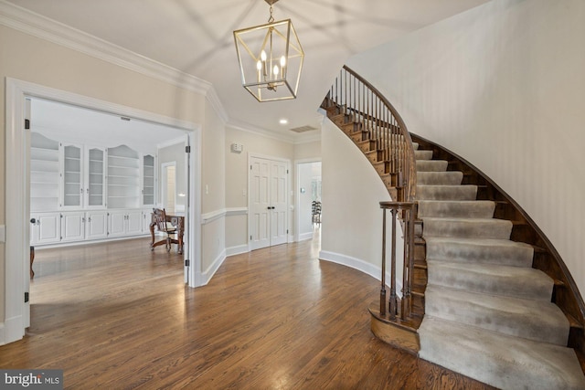 foyer with a chandelier, wood finished floors, visible vents, ornamental molding, and stairway