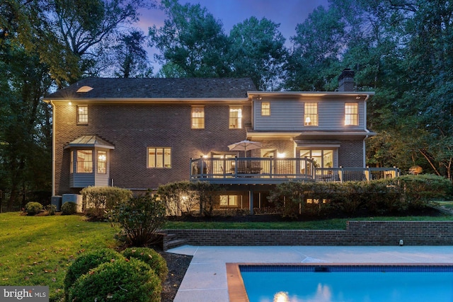 rear view of house with brick siding, a chimney, a lawn, an outdoor pool, and a wooden deck