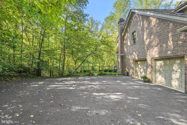 view of property exterior with a garage, brick siding, driveway, and a chimney