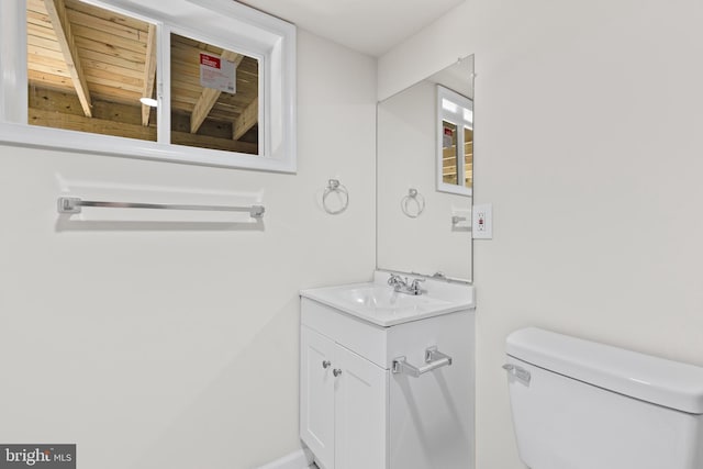 half bath featuring baseboards, vanity, and toilet