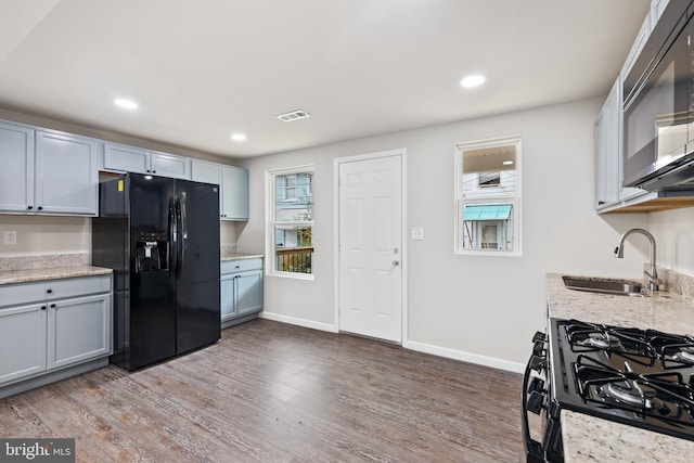 kitchen featuring wood finished floors, a sink, visible vents, baseboards, and black appliances