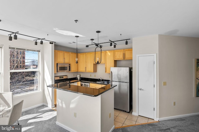 kitchen with light brown cabinets, a kitchen island, dark countertops, appliances with stainless steel finishes, and light colored carpet