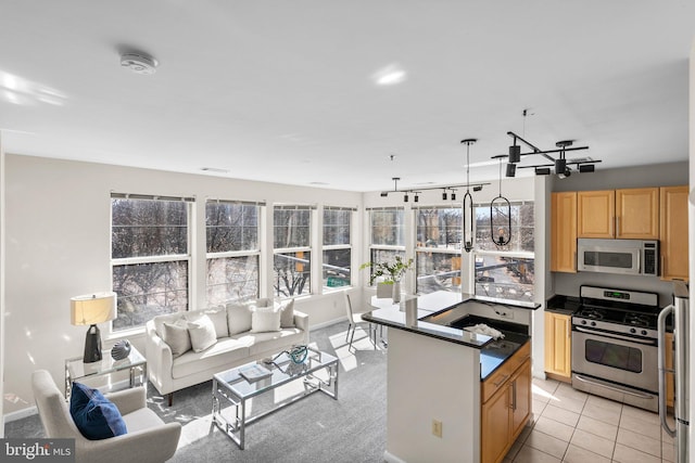 kitchen with light tile patterned floors, light brown cabinetry, stainless steel appliances, dark countertops, and open floor plan