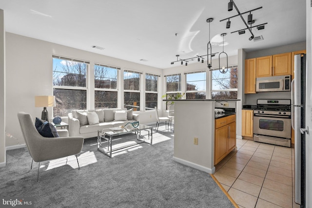 kitchen with light tile patterned flooring, light brown cabinetry, stainless steel appliances, dark countertops, and open floor plan