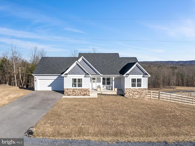 view of front of house with a porch, a garage, a shingled roof, fence, and stone siding