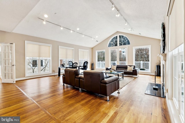 living area with french doors, a fireplace, light wood-style flooring, high vaulted ceiling, and baseboards