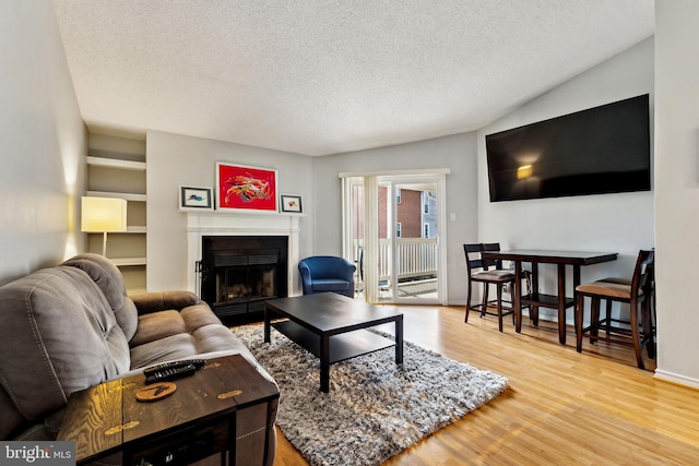 living room with a fireplace with flush hearth, a textured ceiling, and wood finished floors