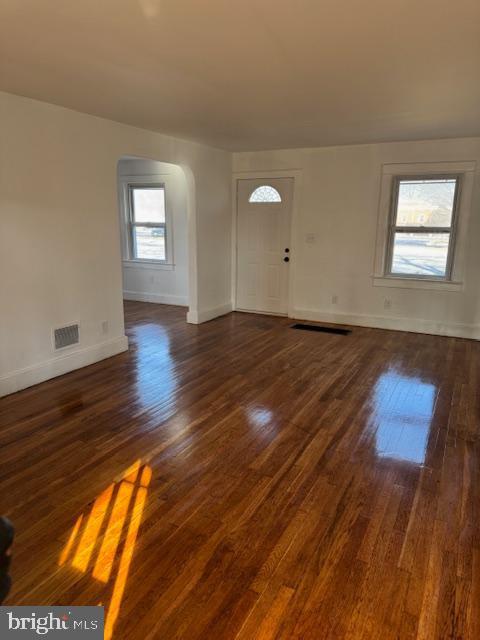 foyer entrance with visible vents, arched walkways, dark wood finished floors, and baseboards