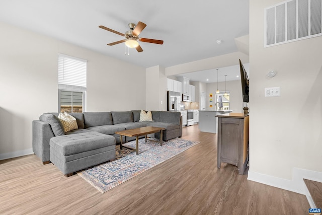 living area with light wood-style floors, visible vents, baseboards, and a ceiling fan