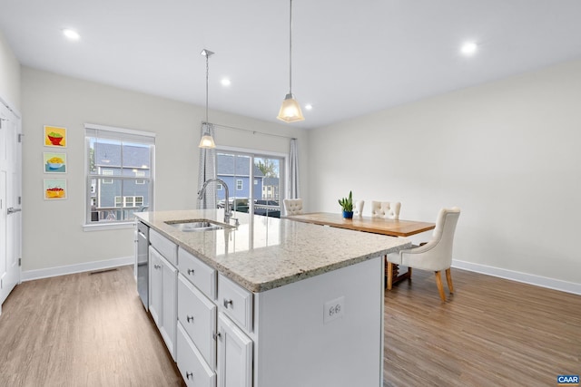 kitchen with a sink, baseboards, stainless steel dishwasher, light wood-type flooring, and a center island with sink