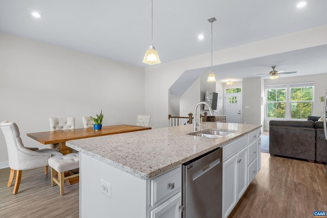 kitchen with a sink, open floor plan, dishwasher, light wood finished floors, and decorative light fixtures