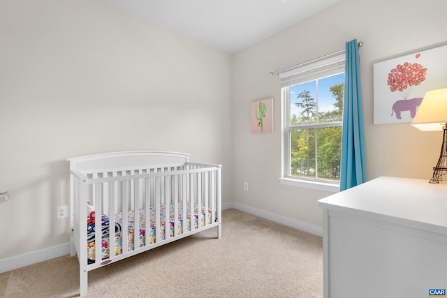 bedroom featuring baseboards, a crib, and light colored carpet