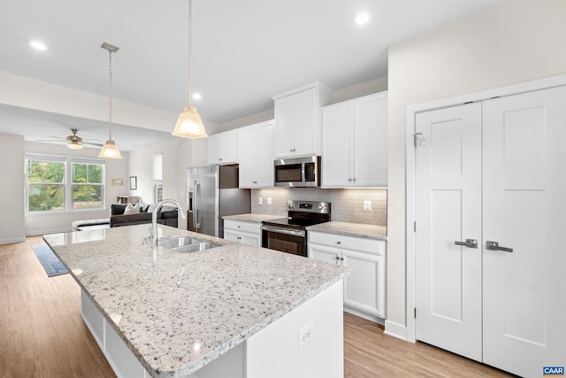 kitchen with stainless steel appliances, a sink, open floor plan, backsplash, and a center island with sink