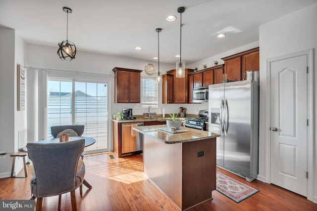 kitchen featuring light stone counters, wood finished floors, hanging light fixtures, appliances with stainless steel finishes, and a center island