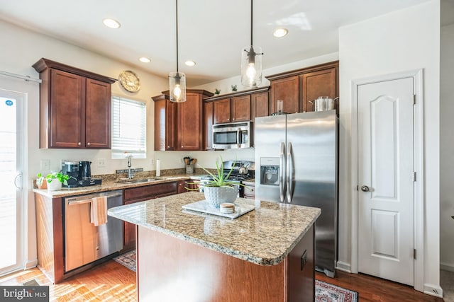 kitchen with appliances with stainless steel finishes, light stone counters, a center island, a sink, and recessed lighting