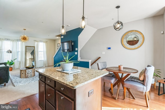 kitchen featuring light wood finished floors, pendant lighting, open floor plan, and dark brown cabinets