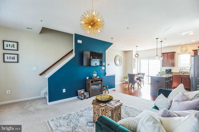 carpeted living room featuring a notable chandelier, baseboards, stairway, and a sink