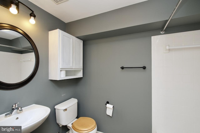 bathroom with visible vents, a shower, a sink, and toilet