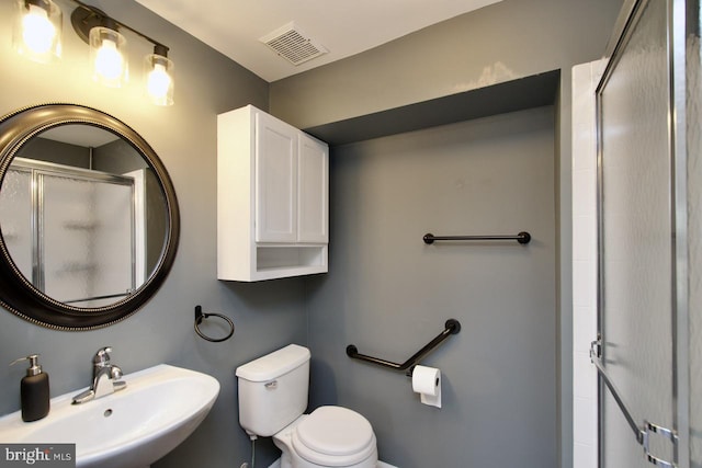 bathroom featuring toilet, a stall shower, a sink, and visible vents