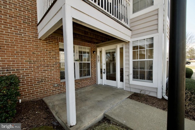 view of exterior entry featuring brick siding, a patio area, and a balcony