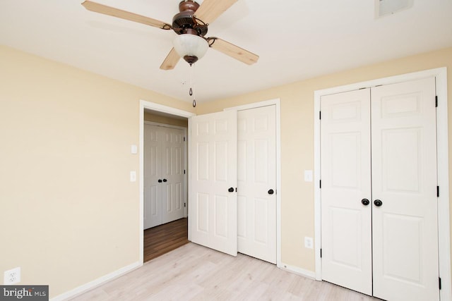 unfurnished bedroom with baseboards, light wood-style flooring, visible vents, and two closets