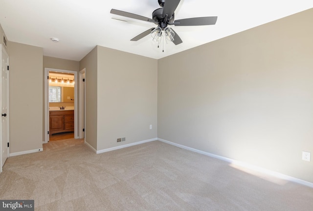 unfurnished bedroom featuring light colored carpet, a sink, ceiling fan, ensuite bath, and baseboards