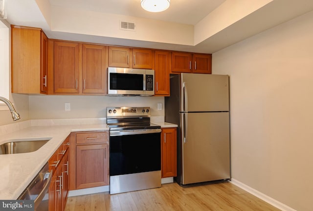 kitchen with visible vents, appliances with stainless steel finishes, brown cabinetry, a sink, and light wood-type flooring