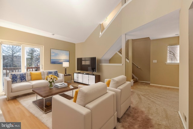 living room with a high ceiling, light carpet, baseboards, and stairs